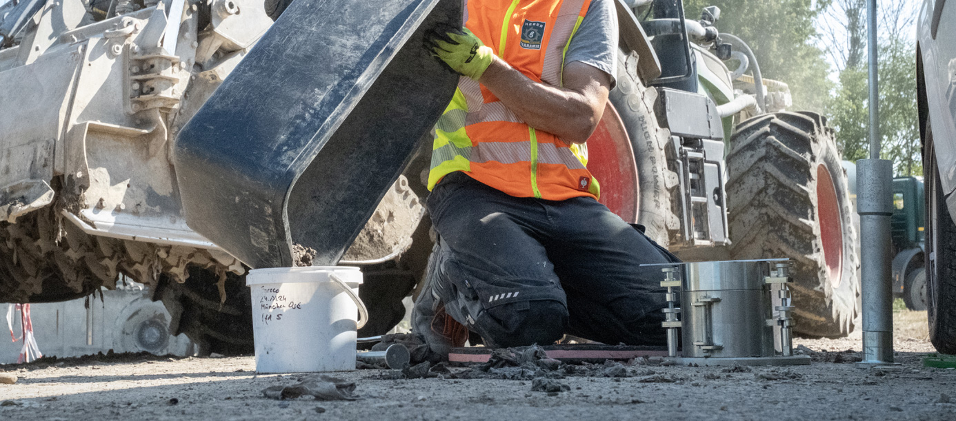 Aufnahme/Foto eines Geologen beim Arbeiten. Er sitzt auf dem Boden und schüttet Bodenproben von einer Wanne in einen Eimer.